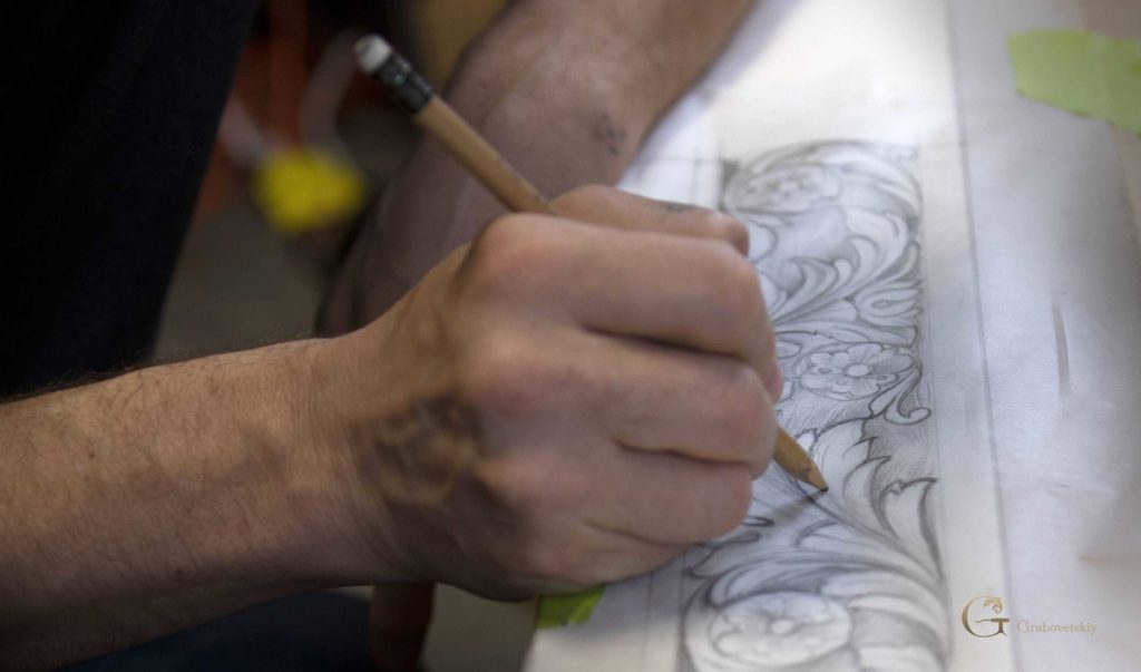 A close-up of a hand drawing a detailed design for wood carving, with a pencil on paper. This image captures the artistic process, perfect for those interested in wood carving classes or lessons. The focus is on the intricate patterns developed before the actual carving begins.