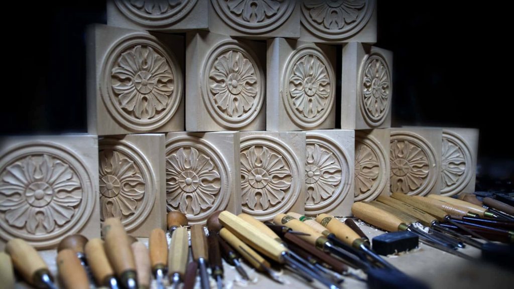 Alt Text: A collection of carved wooden blocks with intricate floral designs stacked together, surrounded by various wood carving tools like chisels and gouges. Perfect for showcasing wood carving classes and lessons, highlighting the craftsmanship involved in this art.