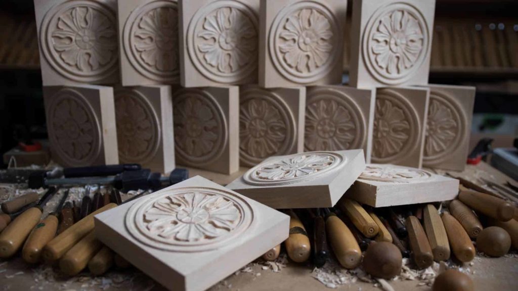 A cozy wood carving workspace featuring beautifully carved floral patterns on wooden plaques, alongside an array of carving tools. This scene perfectly captures the art of wood carving and serves as inspiration for wood carving classes and lessons. Need a hand with your carving? You&rsquo;re in the right place!