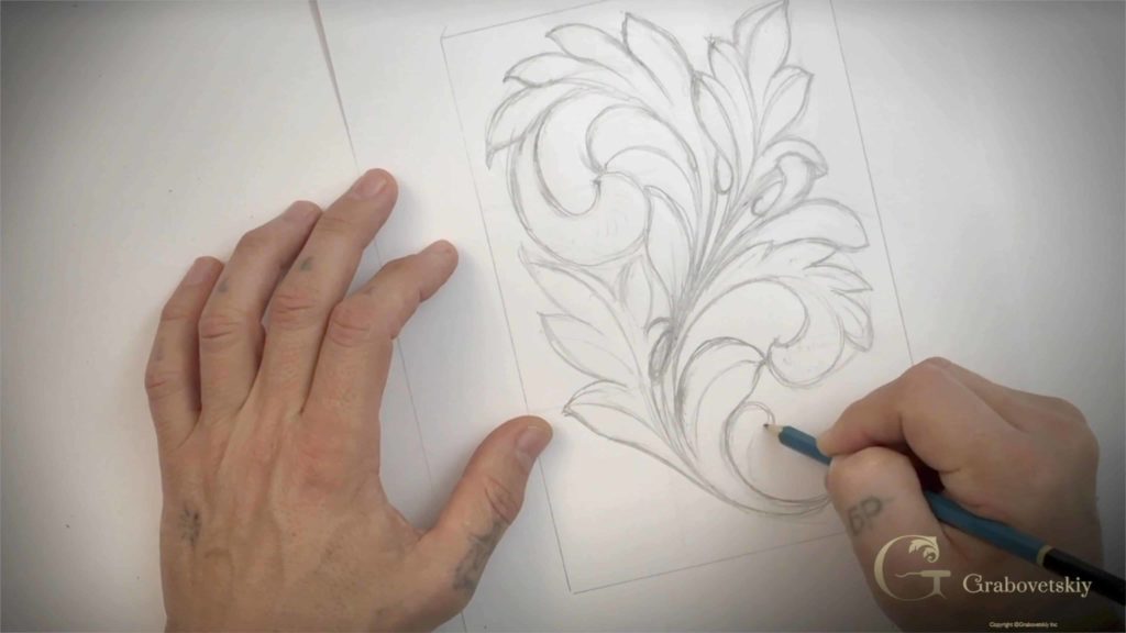 A person is sketching a detailed floral design on paper, preparing for wood carving. Their hand grips a blue pencil tightly, as they focus on the curves and lines of the drawing. You can see some marks on their fingers, hinting that this isn’t their first sketch. This image captures the early stages of wood carving classes, where planning is key before diving into the actual carving process. Wood carving lessons kick off with sketching, and it looks like they’re on the right path to creating something beautiful!!!