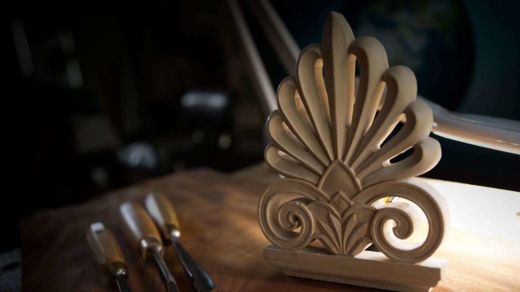 A beautifully carved wood piece showcasing intricate details, sitting on a workbench. Next to it are some trusty carving tools with wooden handles, perfect for any wood carving classes or lessons.