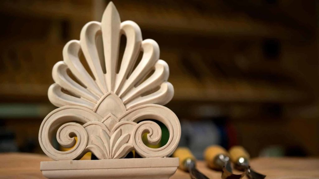 Alt text: A beautifully carved wooden ornament featuring intricate details, displayed prominently on a workbench. In the background, various wood carving tools are ready for use, emphasizing the atmosphere of wood carving lessons and classes where skills are honed.