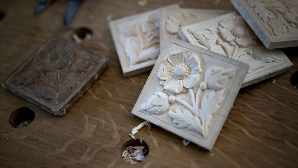 Close-up of intricately carved wood pieces showcasing floral designs, resting on a wooden workbench with shavings scattered around. This image illustrates the beauty of craft and the skills developed in wood carving classes and lessons. Perfect for anyone interested in the art of wood carving!