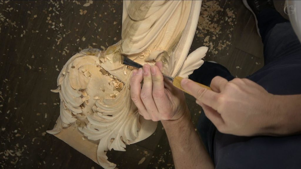 A close-up shot of a wood carver delicately working on a detailed piece, surrounded by wood shavings. The person is using a chisel to sculpt intricate designs, highlighting the artistry involved in wood carving. This image represents the essence of wood carving classes and lessons, showcasing the tools and techniques used by enthusiasts.