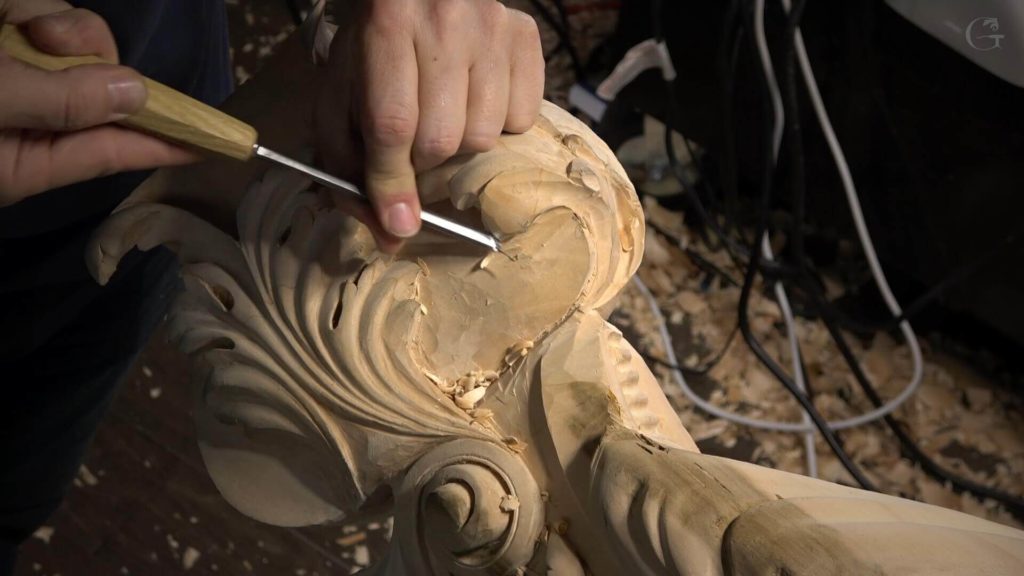 Close-up of a person carving intricate details into a wooden piece using a chisel. Shavings scatter around, showing the process of art in progress. Perfect for anyone looking to join wood carving classes or lessons!