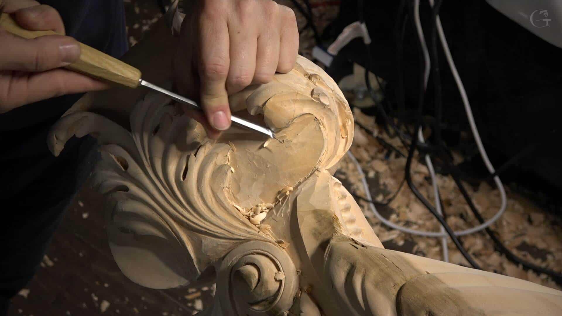 Close-up of a person carving intricate details into a wooden piece using a chisel. Shavings scatter around, showing the process of art in progress. Perfect for anyone looking to join wood carving classes or lessons!