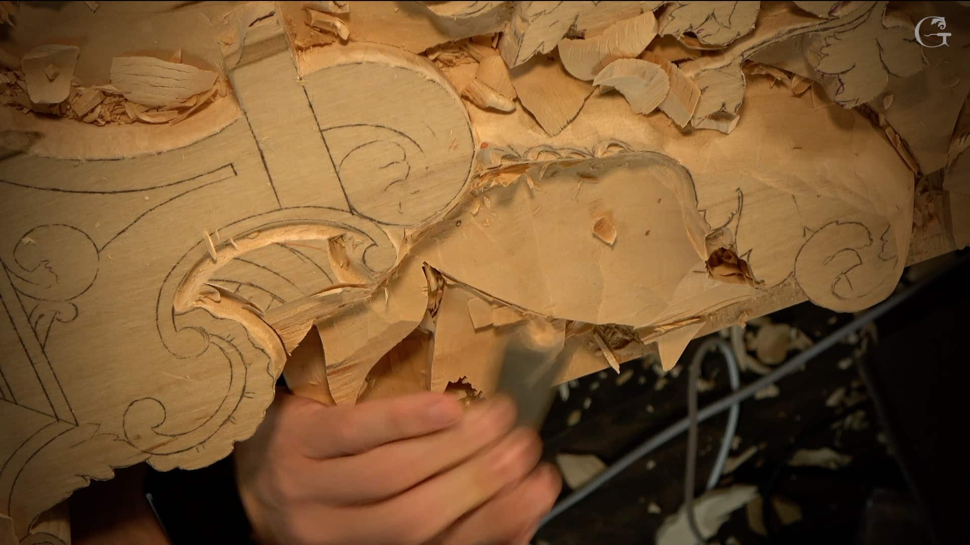 WOODCARVING LESSONS: Close-up of Woodcarver Grabovetskiy carving detailed patterns into wood with a chisel. Wood shavings are scattered around the workspace. - Wood Carving tutorials