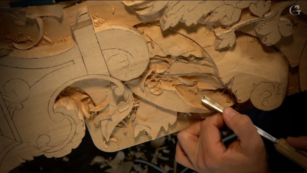 Close-up of wood carving in progress, showing intricate designs on a wooden surface. The image features a person's hand holding a carving tool, precisely shaping the wood. Surrounding the area are wood shavings, highlighting the carving process. This is a glimpse into wood carving classes where beginners can learn and enjoy hands-on wood carving lessons.