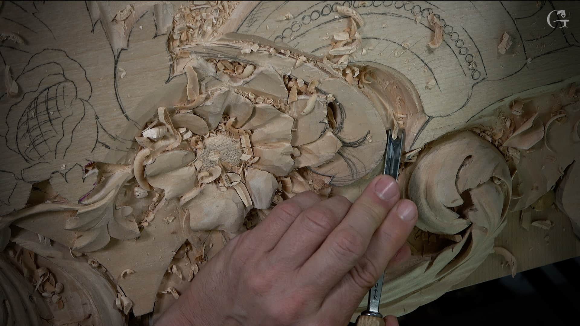 WOODCARVING LESSONS: Close-up of Woodcarver Grabovetskiy's hand using a chisel to carve a detailed flower design into wood, with wood shavings all around. - Wood Carving tutorials