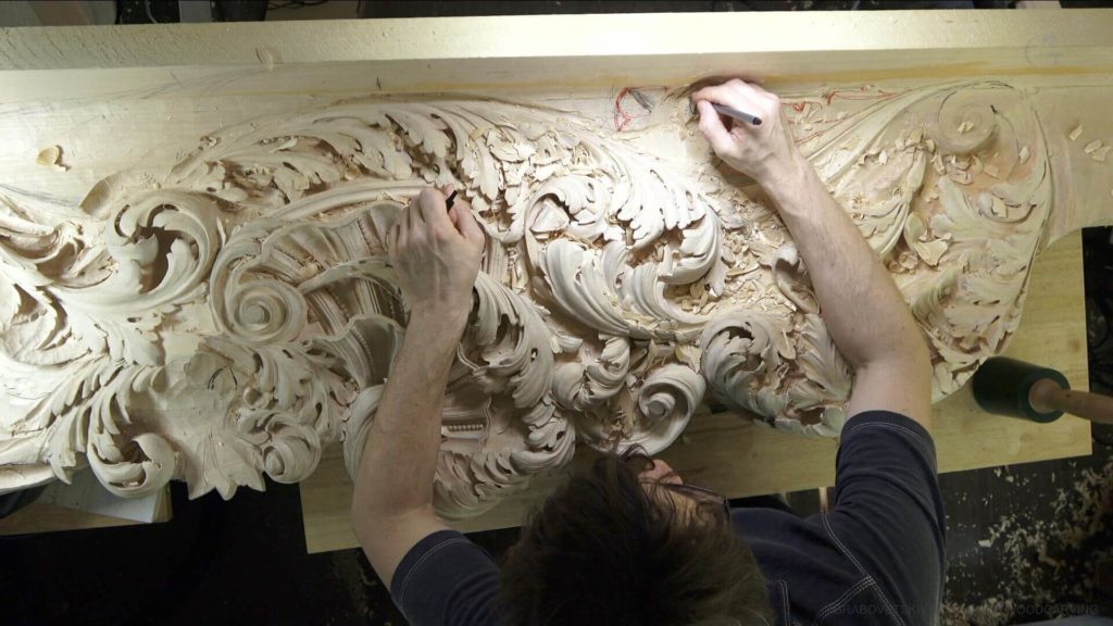 A person is focused on intricate wood carving, showcasing a beautiful, detailed swirl design. They're using tools like a chisel and mallet, working on a large piece of wood. The workbench is covered in wood shavings, reflecting the artistry and effort involved in wood carving classes and lessons.