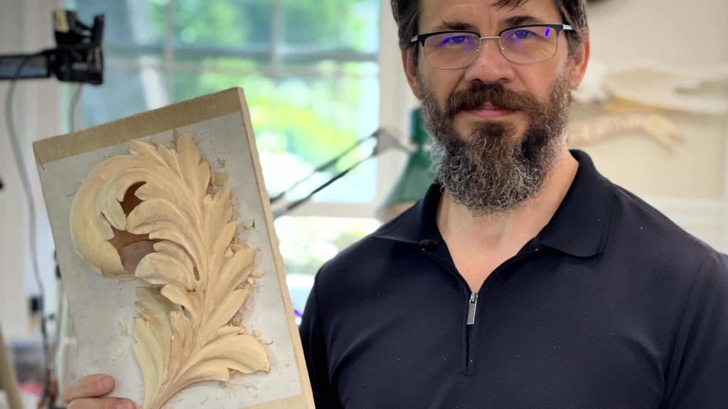 A person holds a carved piece of wood featuring an ornate leaf design, showcasing their wood carving skills. This image represents the art of wood carving, perfect for those interested in wood carving classes and wood carving lessons.