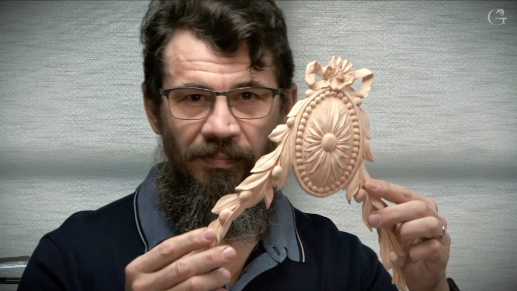 A person holding a beautifully detailed wood carving piece, showcasing intricate floral designs and leaves, with a focused expression. This image highlights the dedication and skill involved in wood carving, which you can learn about in various wood carving classes and wood carving lessons.