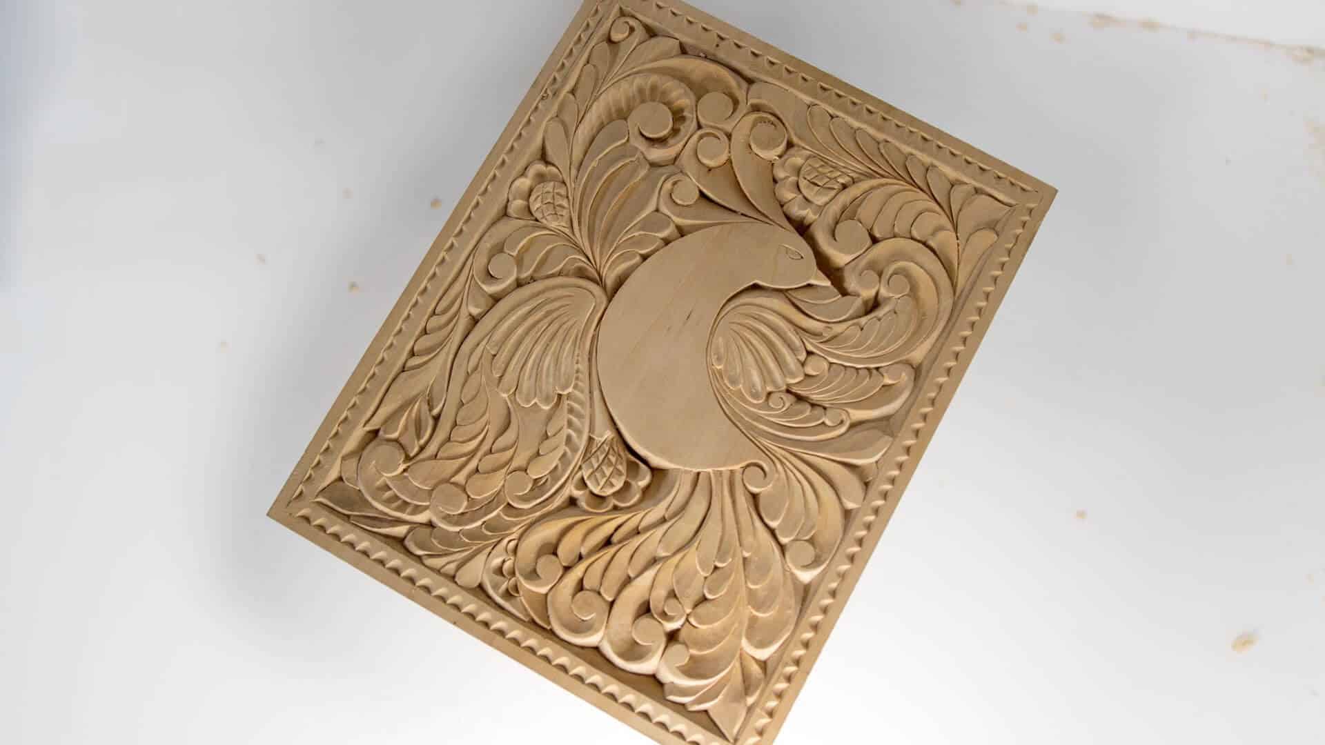 Alt text: A beautifully crafted wood carving featuring intricate patterns with a peacock design, showcasing artistic skills from wood carving classes and lessons.
