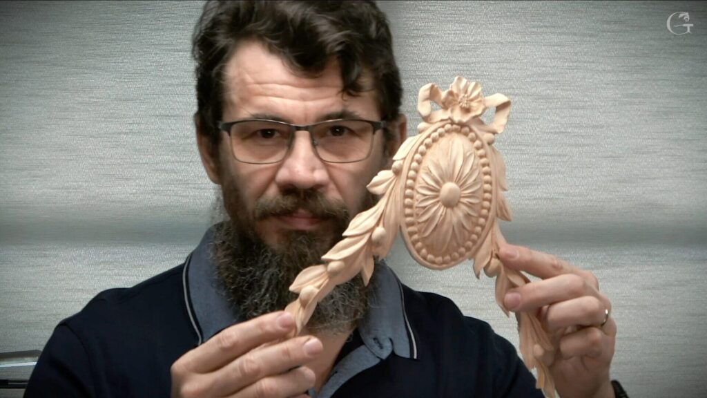 A person holding a beautifully carved wooden piece featuring floral details and intricate designs. The individual appears enthusiastic about wood carving and is likely sharing knowledge from his experience in wood carving classes and lessons.