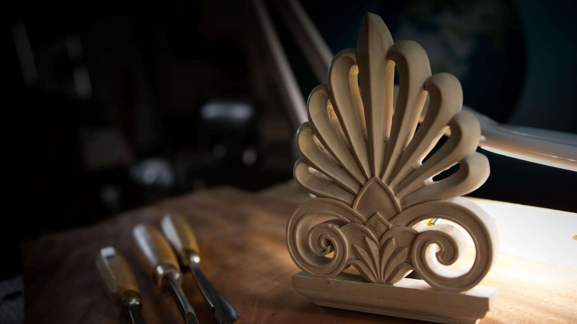 Alt text: A beautifully carved wooden piece showcasing detailed scrollwork, placed on a workbench surrounded by carving tools. This image highlights the craftsmanship involved in wood carving lessons and classes, perfect for aspiring artisans looking to hone their skills.