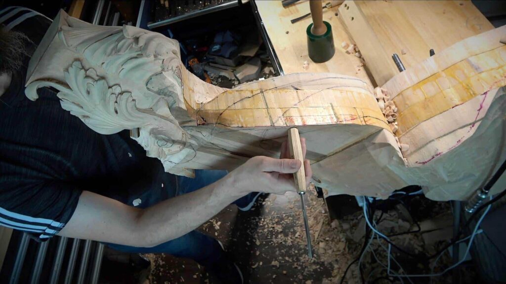 A person carving intricate designs into a piece of wood while holding a compass. Wood shavings and carving tools for beginners are scattered around, inspired by woodcarving tutorials online.