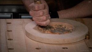 A hands-on view of wood carving, showing a person using a mallet and chisel to create detailed designs in wood. The scene captures the focus and skill involved in wood carving classes and lessons. The workbench is filled with tools, and intricate patterns are taking shape in a piece of fresh wood, emphasizing the craftsmanship and dedication required in this art form. Perfect for those interested in learning the art of wood carving!