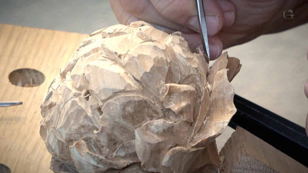 WOODCARVING LESSONS: Woodcarver Grabovetskiy using a chisel to carve details into wood. Close-up of his hands working on a wooden sculpture with various carving tools. - Wood Carving tutorials