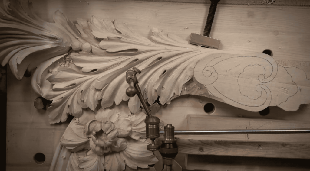 WOODCARVING LESSONS: Close-up of a detailed wood carving in progress. It is held with clamps and guided by a pointing machine. The design shows ornate leaves and floral patterns crafted by Woodcarver Grabovetskiy. - Wood Carving tutorials