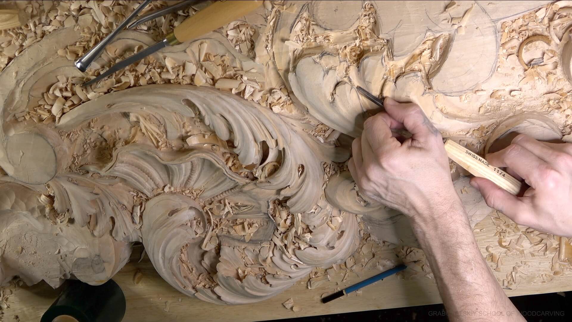 WOODCARVING LESSONS: In a woodcarving lesson, Woodcarver Grabovetskiy carves detailed patterns into wood. Carving tools and wood shavings are visible around his workspace. - Wood Carving tutorials Wood Carving Classes in Falls Church, DC