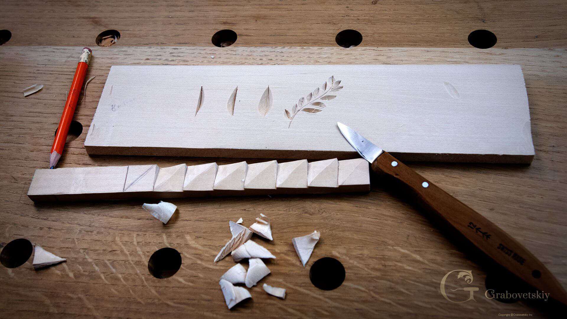 Practice board with three carved leaf shapes and a leafy stem, a carved molding strip, chips and a carving knife on the bench