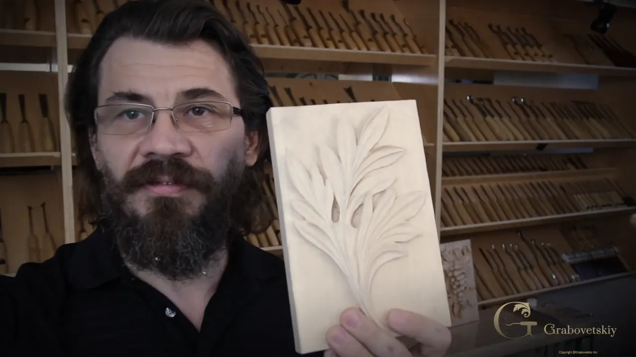Alexander holds the finished panel to the camera with one hand, and the shop wall behind him is racked with gouges.