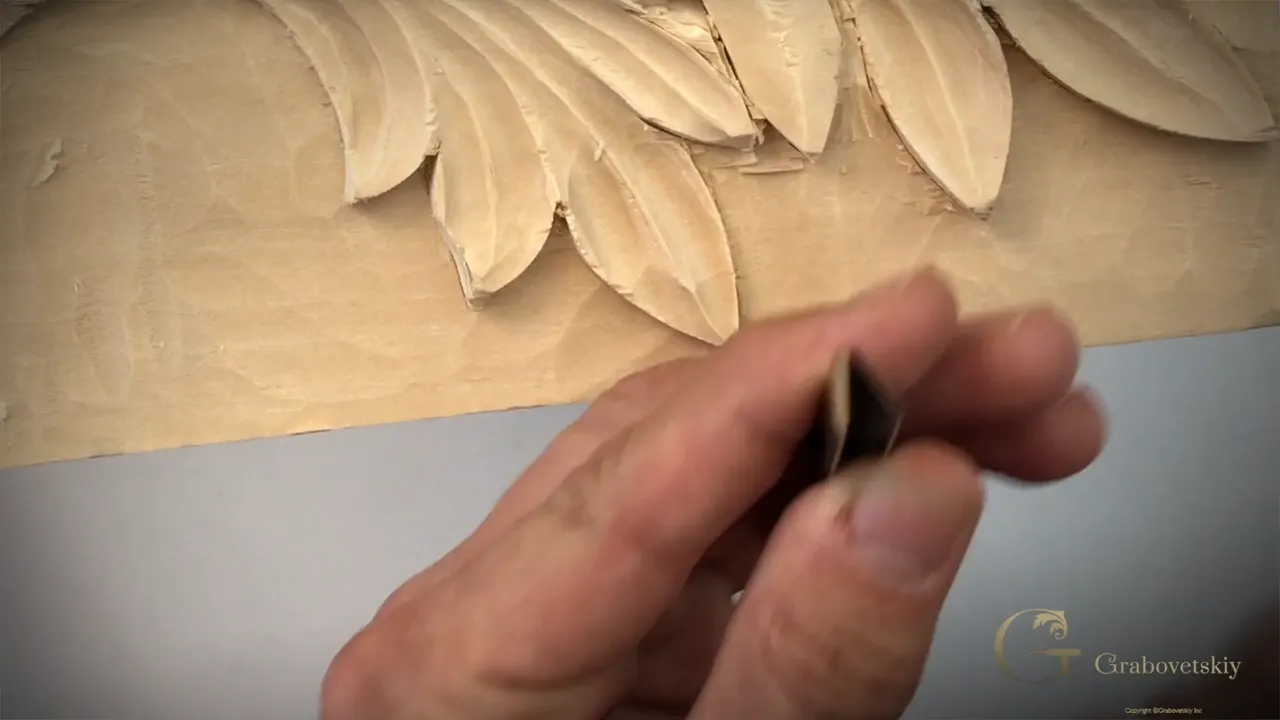 Narrow V tool, held up beside the carved lobes so its grinding angle shows.