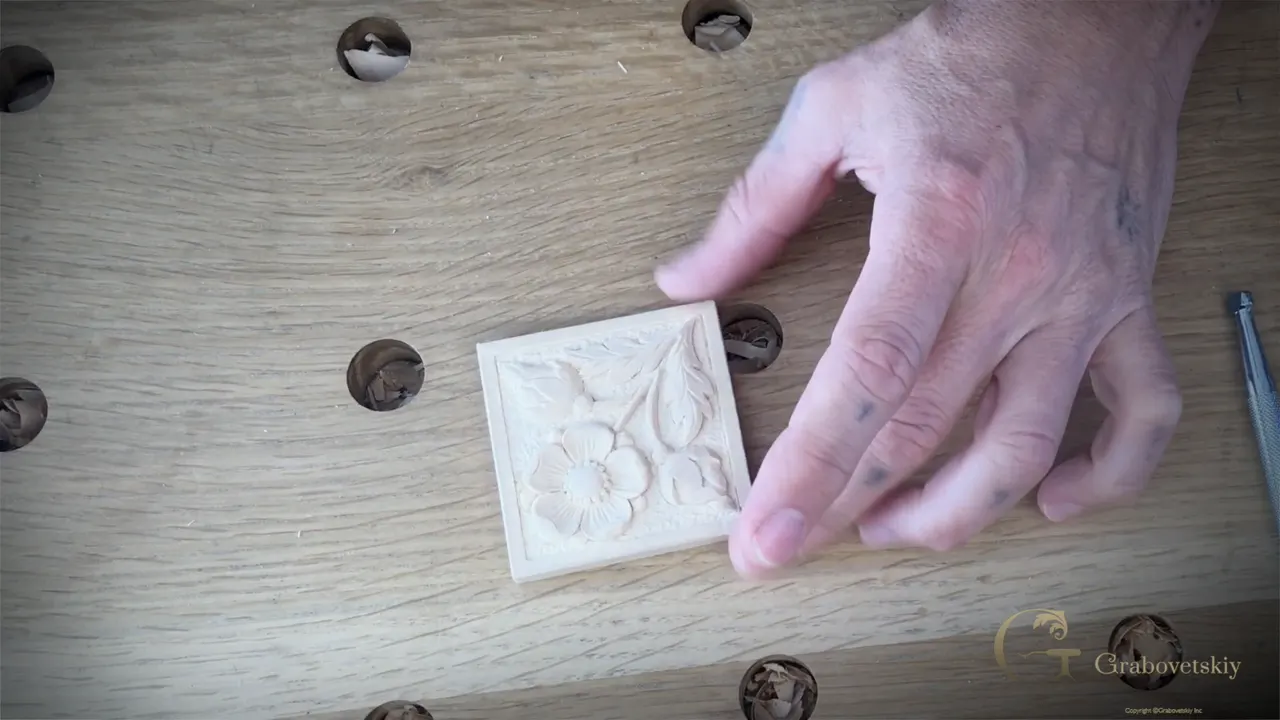 Finished rosette in basswood lying on the bench, flower and leaves inside a raised square border.