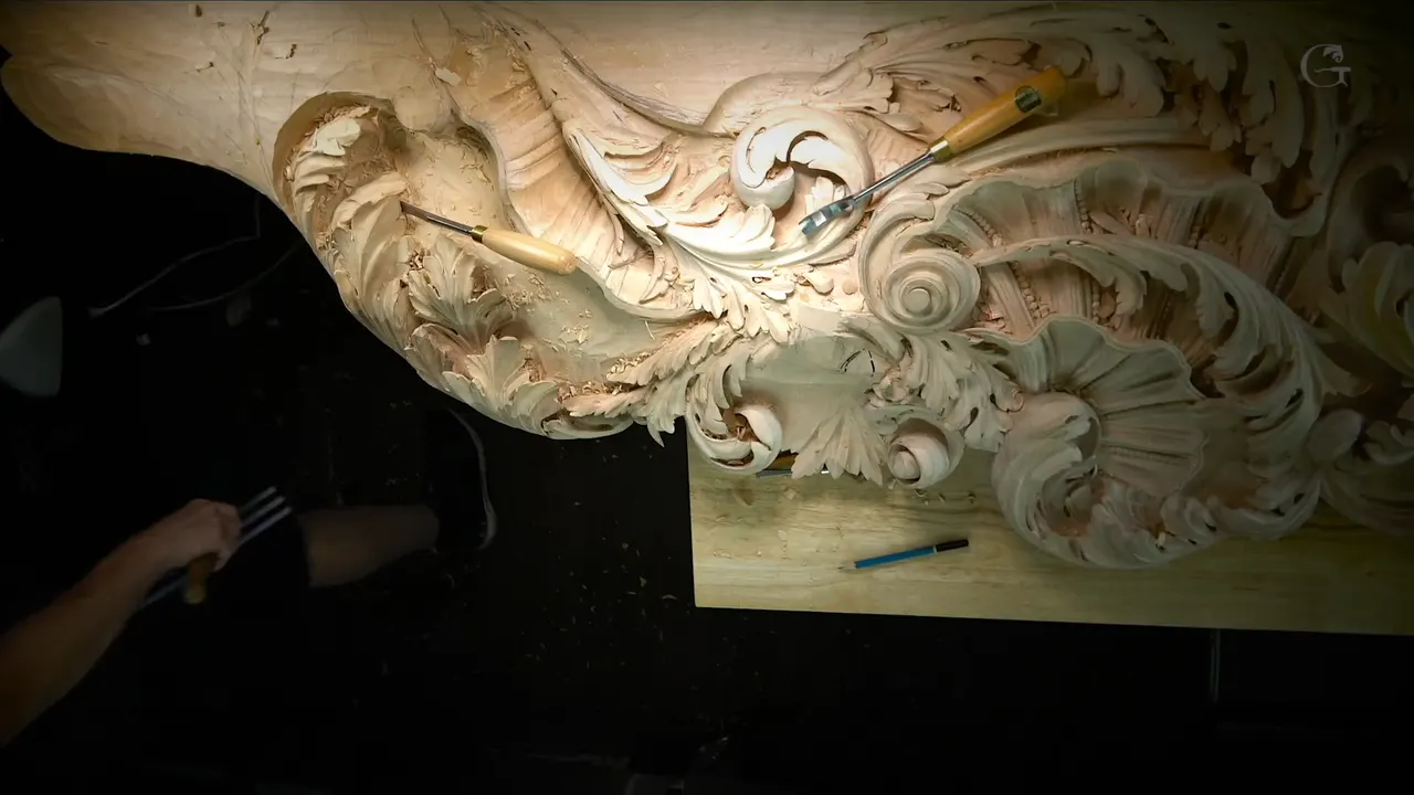 Whole ceiling panel under a lamp, two carving gouges resting on its acanthus scrolls and one arm at left