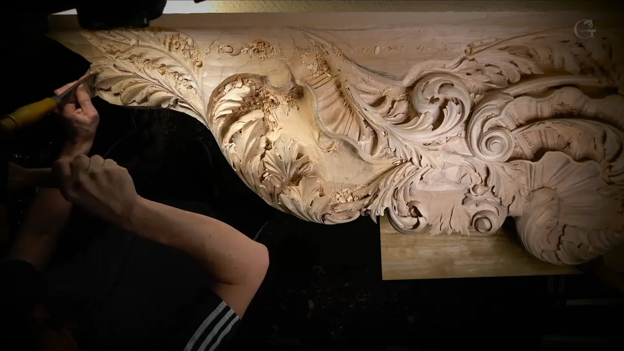 A carver's arms reach across a long carved panel with scrolls, a shell and acanthus leaves