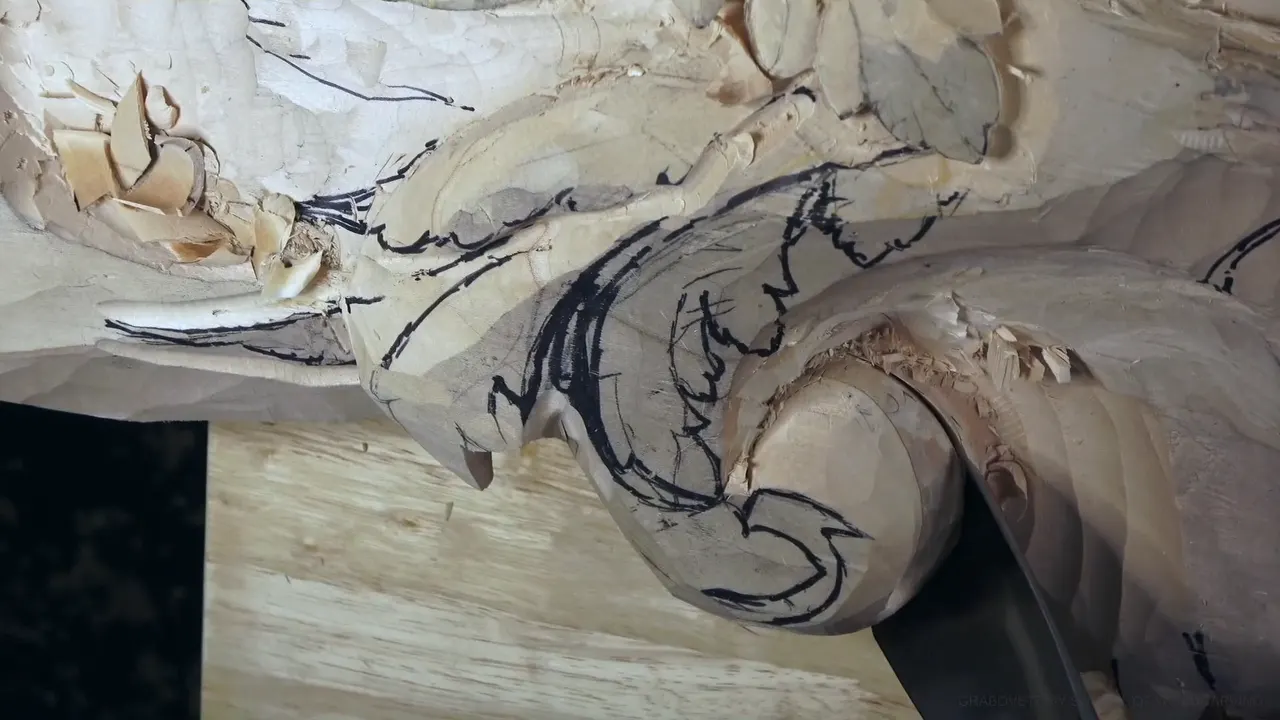 A wide gouge sits deep in the round end of a carved acanthus head, marker lines on the leaf above.