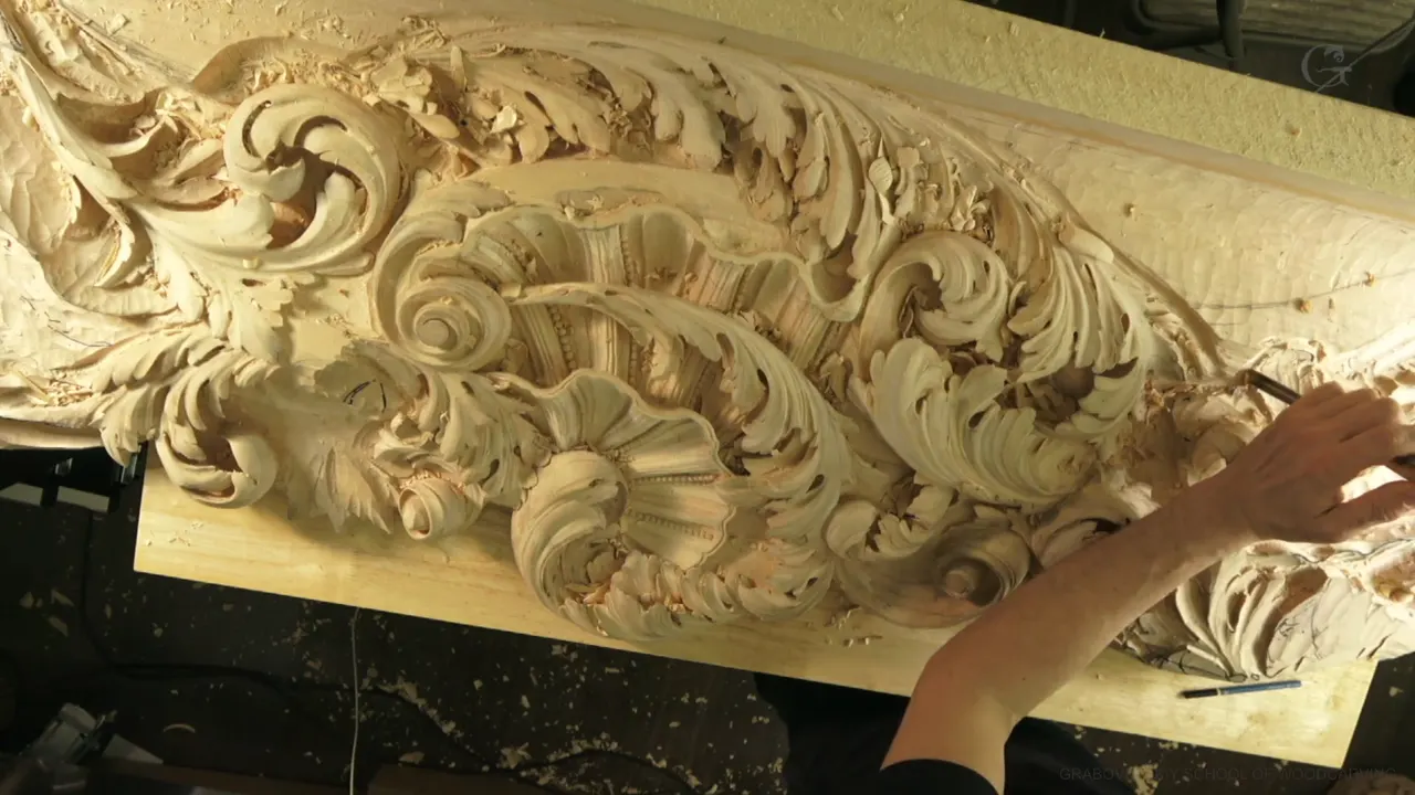 Carved acanthus scrolls around a shell, seen from above, one hand working at the right edge