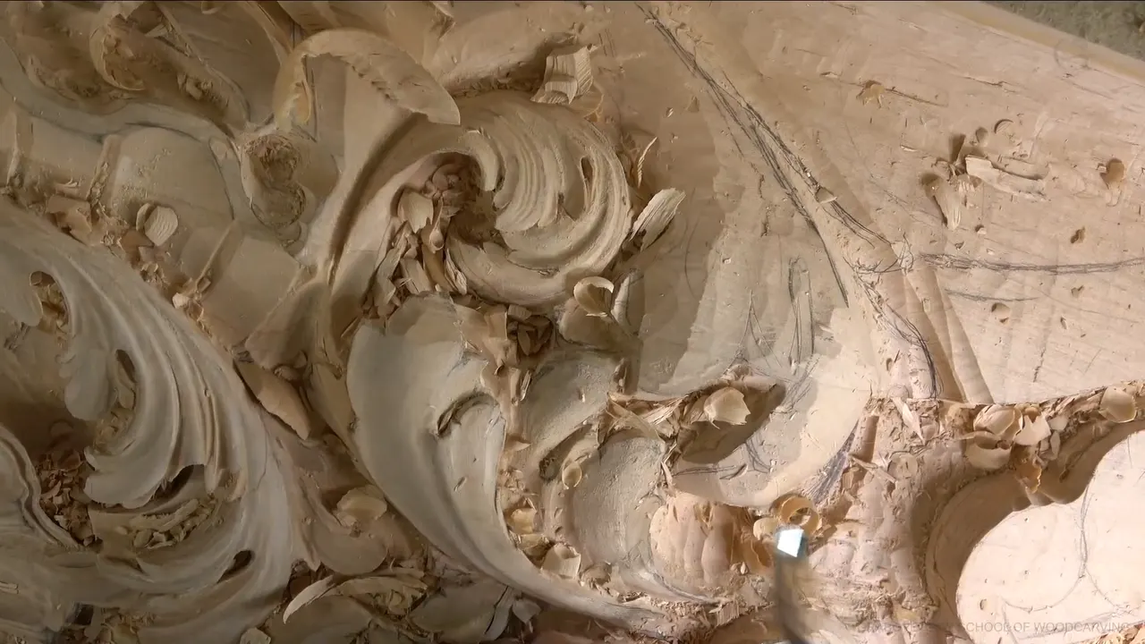 Wide view of the carved board, acanthus scrolls curling across it, chips still lying in the hollows.