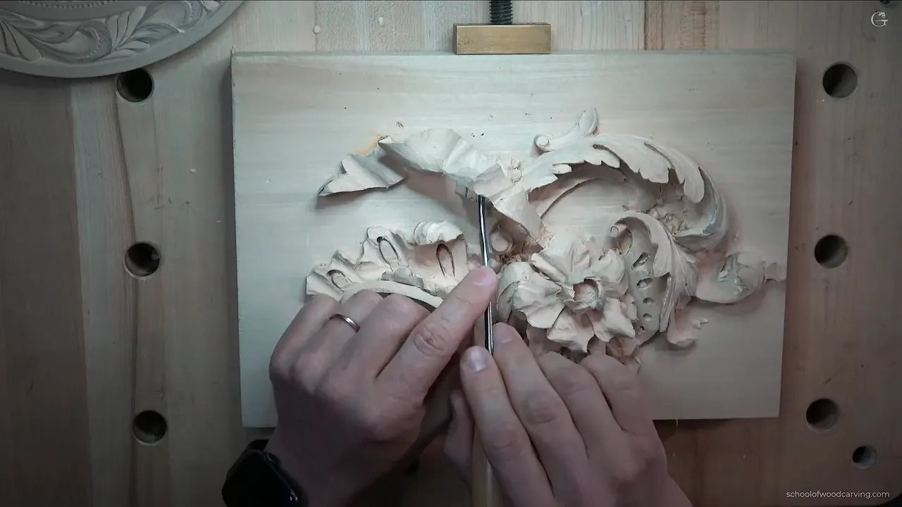 Back bent gouge laid across the carved panel, the backward curve of its blade clear from the side.
