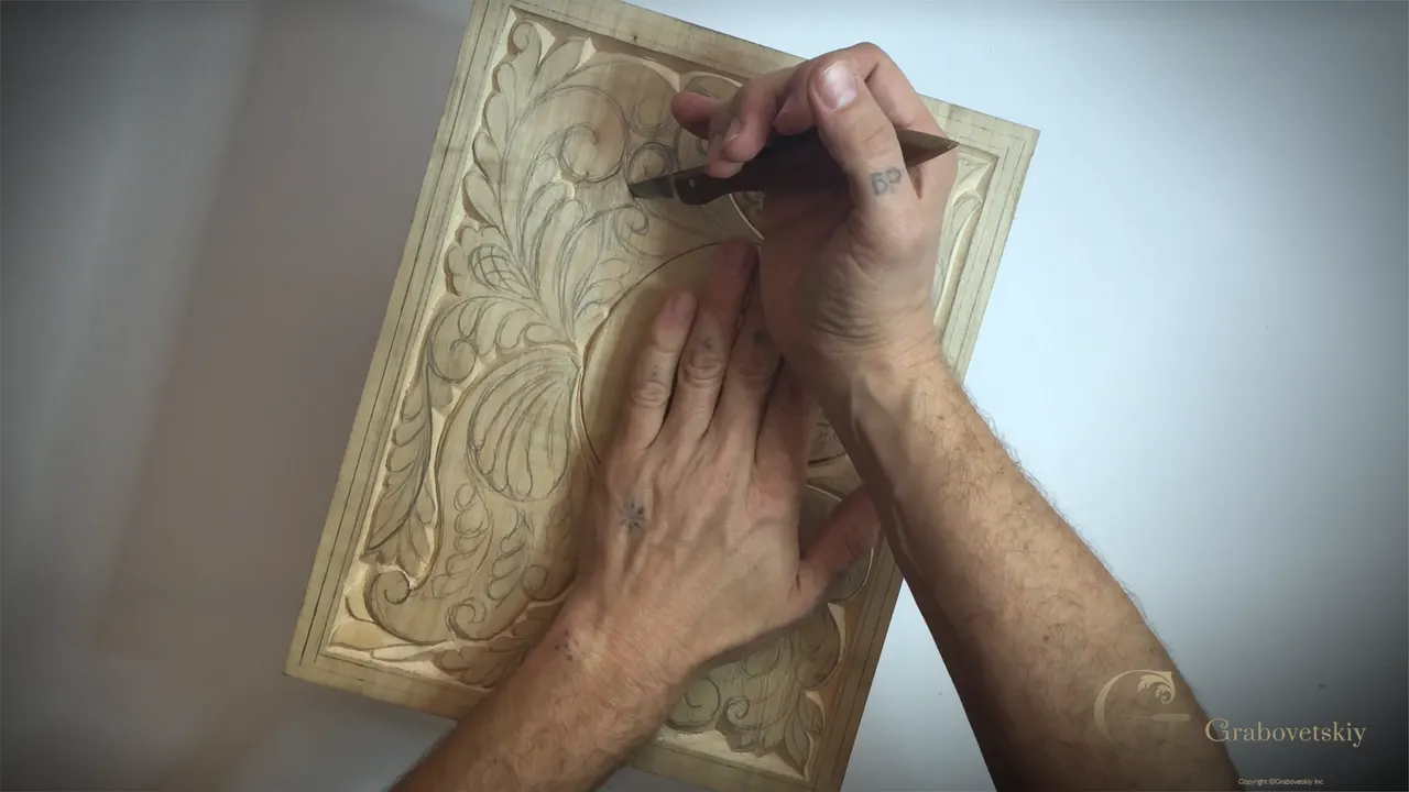 Carving hand pressed down on a basswood panel, the knife handle buried in the palm.