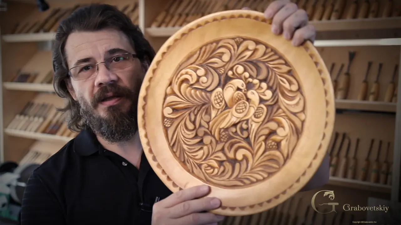 A round dish carved in the curly style, held up in front of a rack of carving tools.