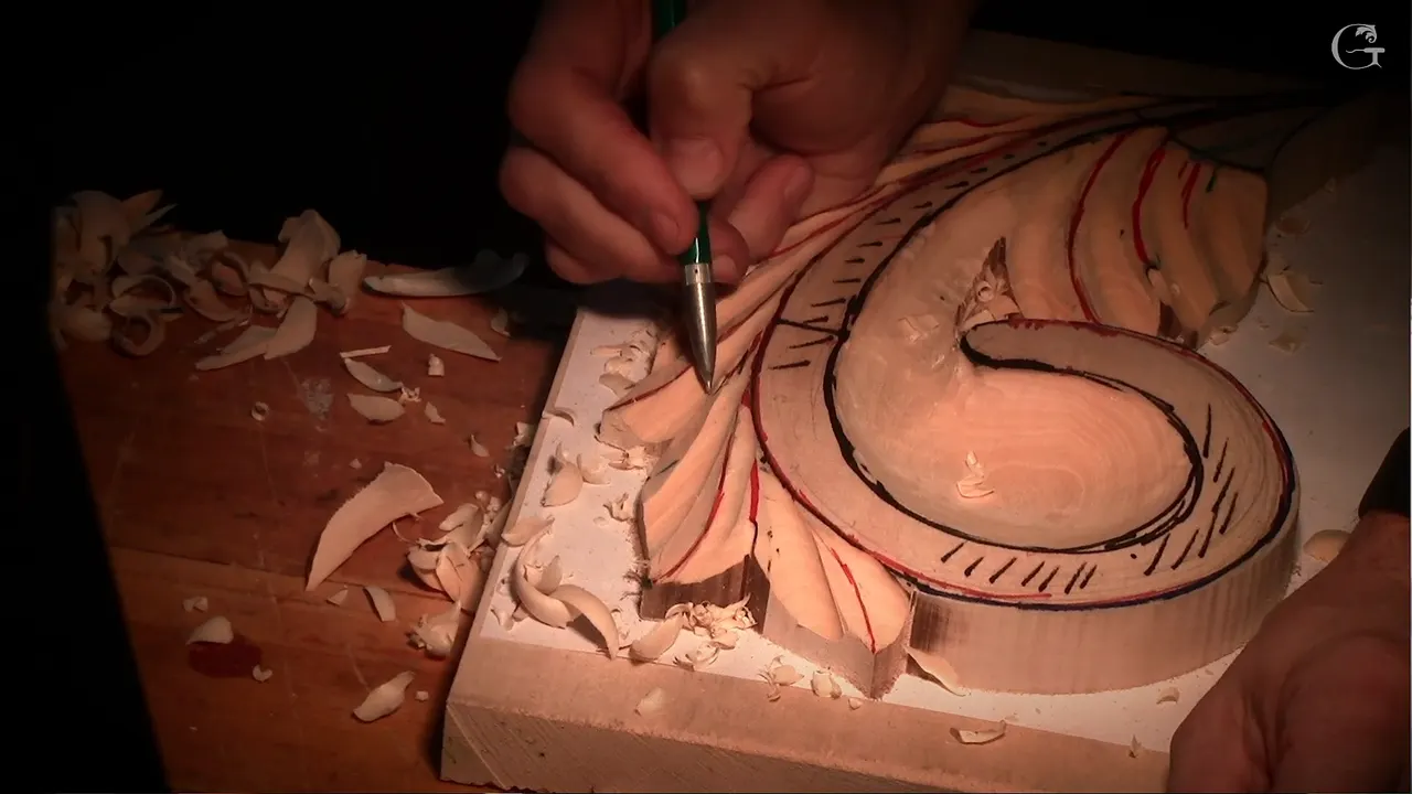 Fine tool held like a pen over the carved leaf, red and black lines still showing