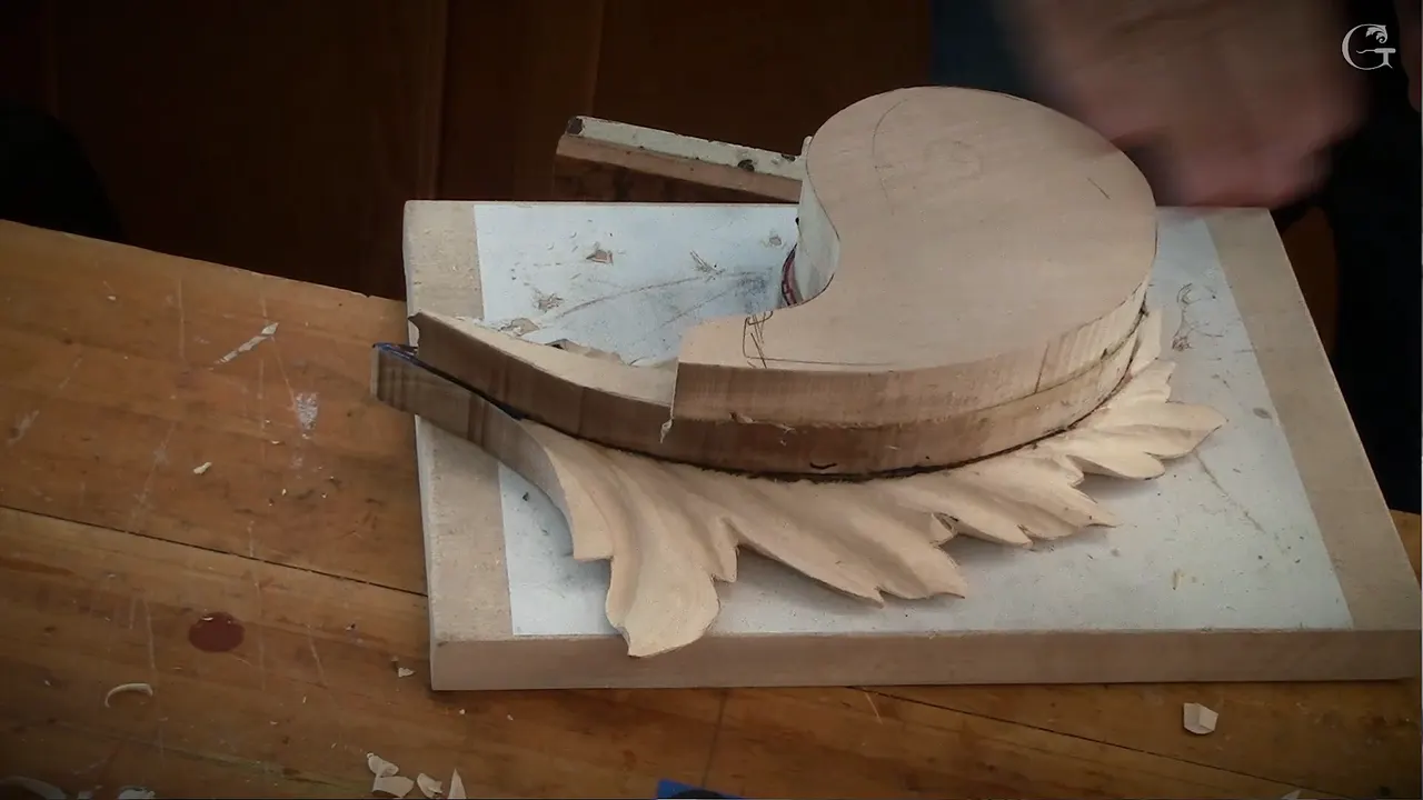 Three glued boards stacked into one leaf, a hand steadying the top disc while the carved acanthus runs out below