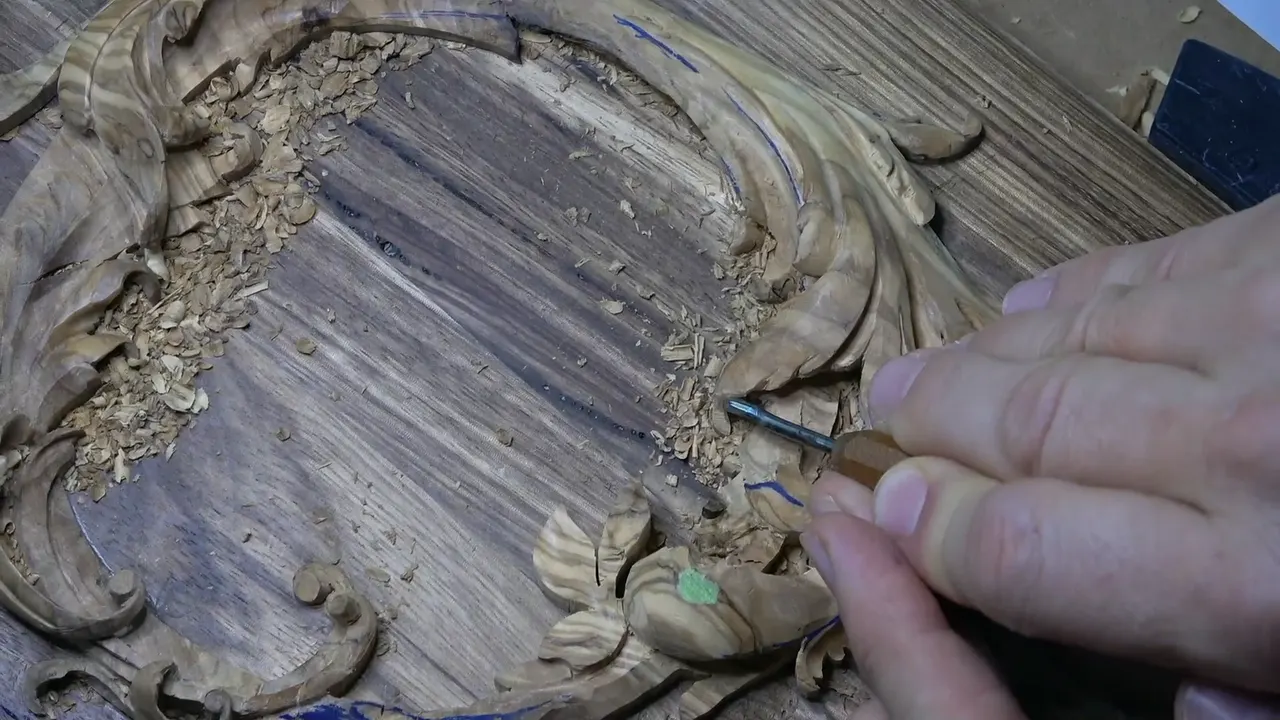 Olive acanthus curling around a dark acacia lid, chips inside the ring, a hand pushing a short gouge into the leaves