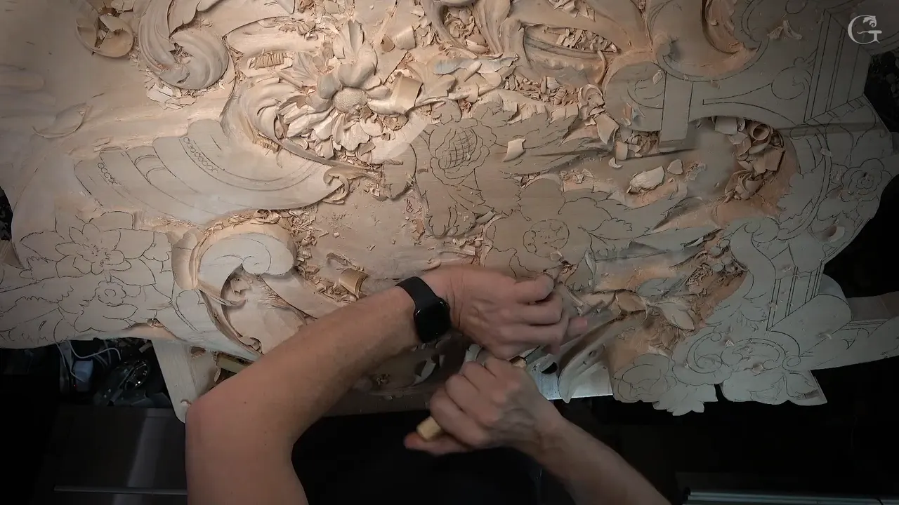 Overhead view of the whole panel, both hands at a gouge among roughed leaves