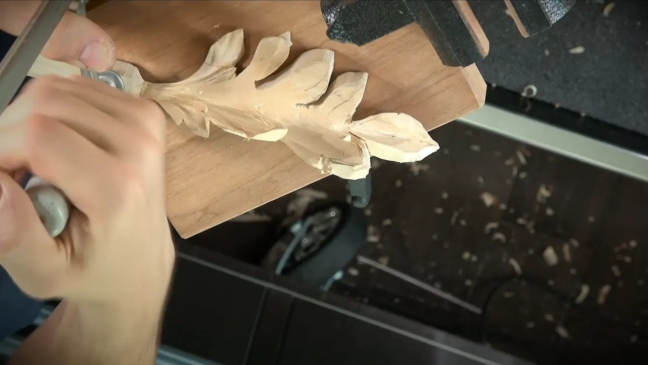 Carved leaves turning different ways on a clamped piece, gouge in hand