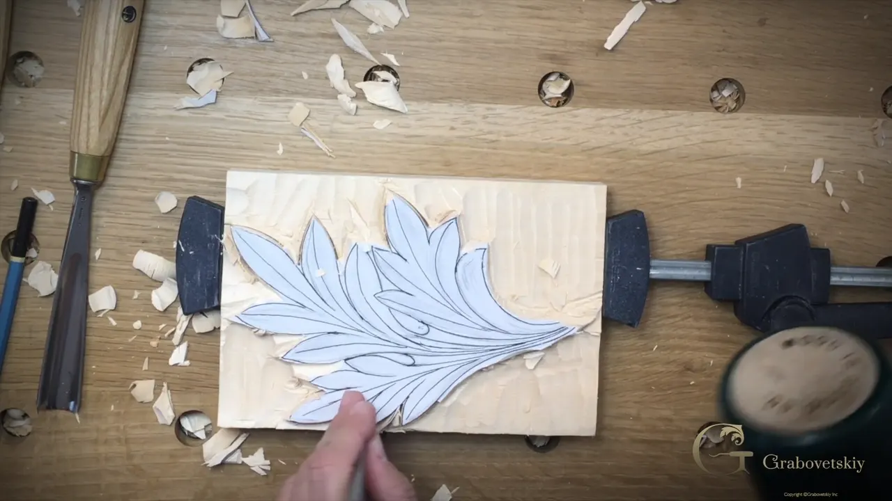 A gouge at the edge of the outlined leaf, a mallet resting behind the clamp