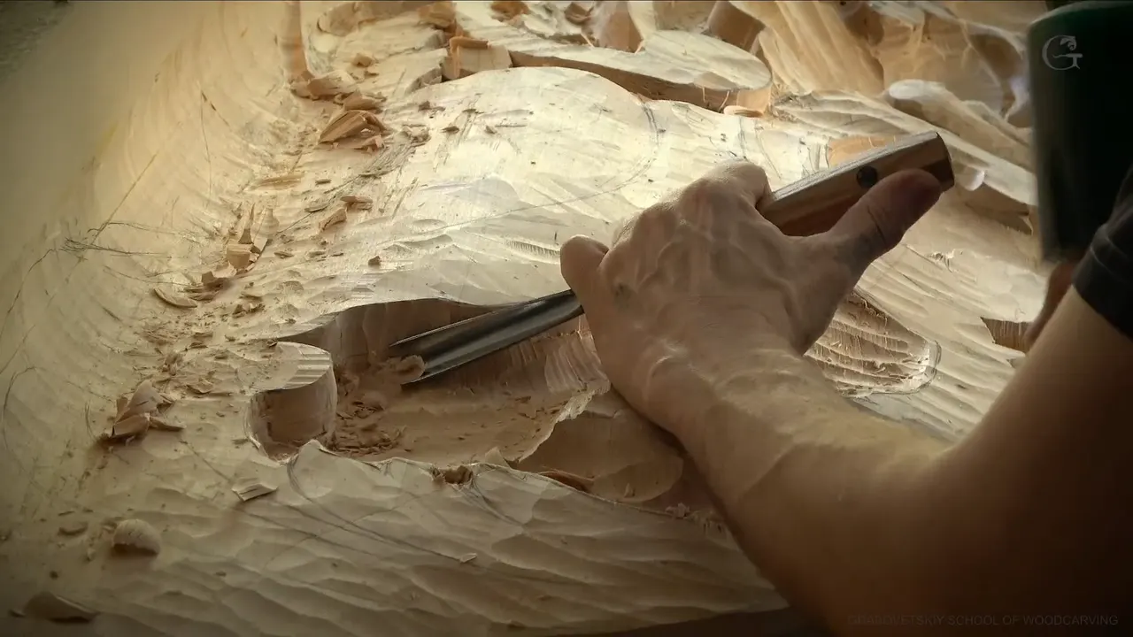 A hand drives a long gouge into a deep pocket while the green mallet waits above it