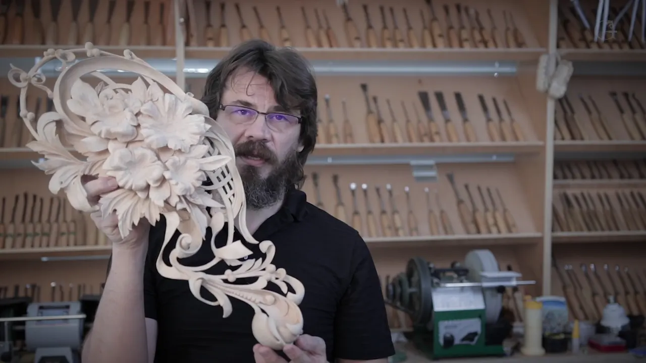 Alexander holding the finished carved panel of flowers, basket weave and scrolls in front of his tool wall