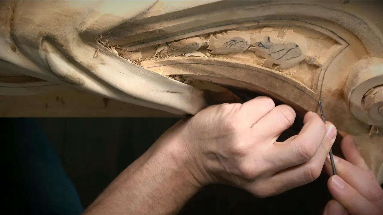 Two hands guide a thin veiner along the curved lower border of a recessed panel with pencil leaves drawn inside