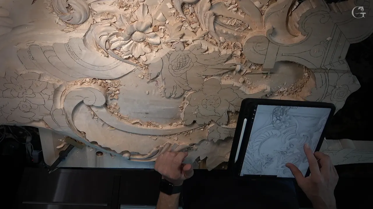 Tablet propped beside the carving with the same drawing on screen, both hands over it