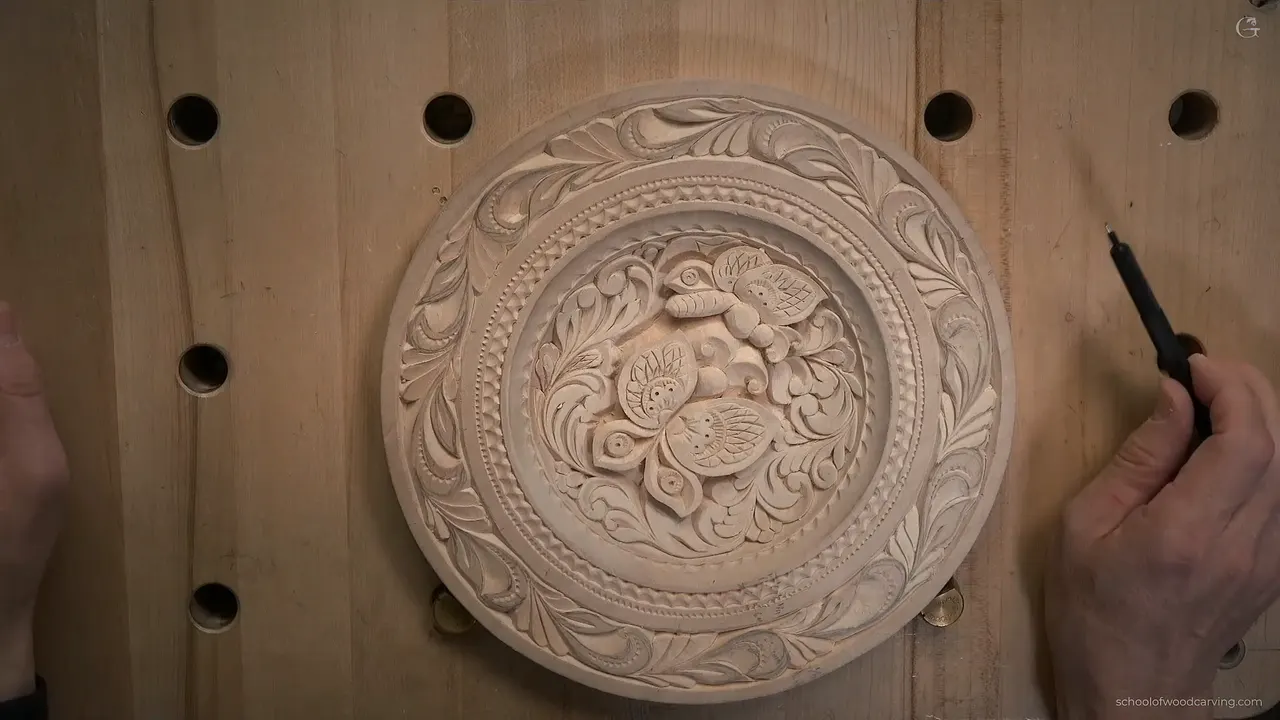 A finished basswood plate with two carved butterflies lies flat on a workbench