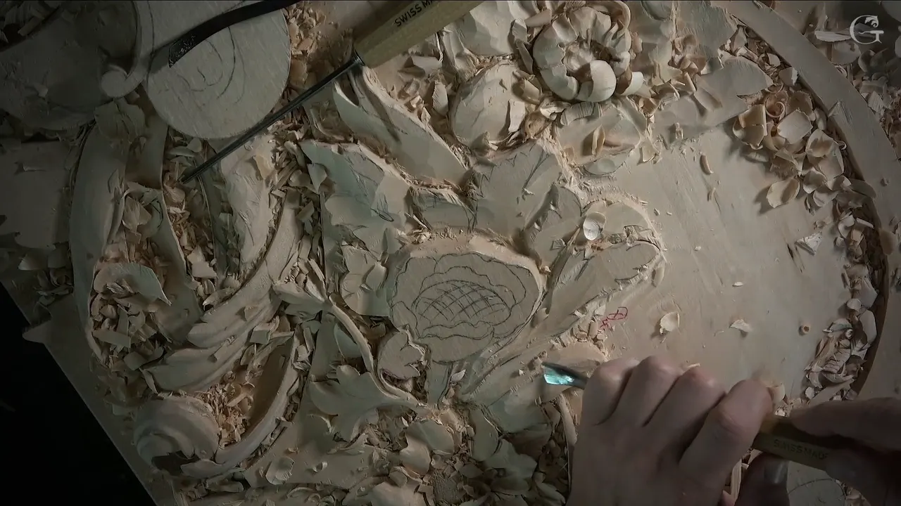 The panel from above, one hand bringing a small tool to the lower right of the gridded flower