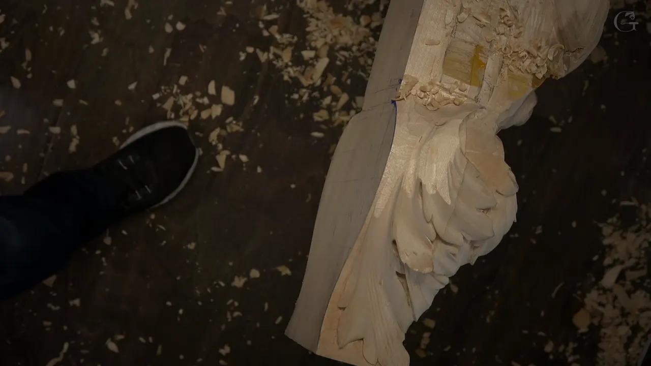 Overhead view of the half-carved middle of the block, leaves at one end and a sneaker on the dark floor.
