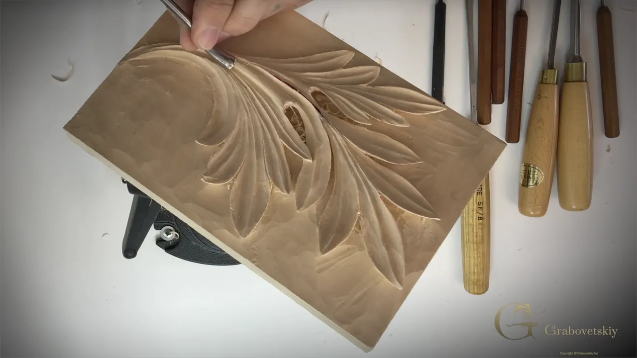 The panel laid flat on the white bench with the leaf cut and a row of gouges beside it.